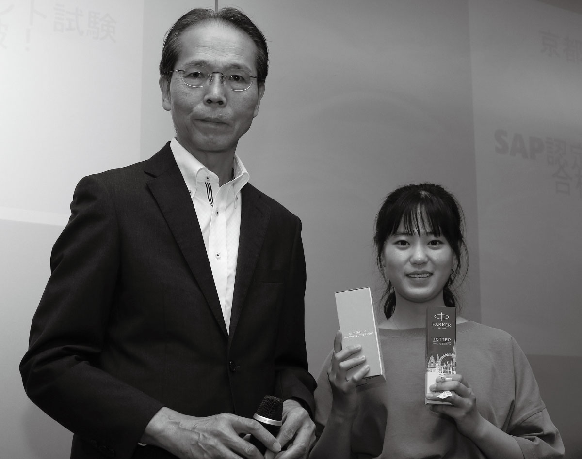 KCGIからのSAP認定試験合格者150人目となった胡さん。藤原正樹教授からSAPジャパンの記念品を受け取った。